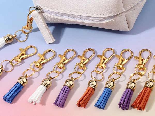 Gold swivel snap hooks with colorful tassels and key rings arranged in front of a white pouch.