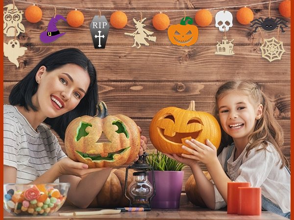 Mother and daughter carving pumpkins for Halloween, with festive decorations hanging above.
