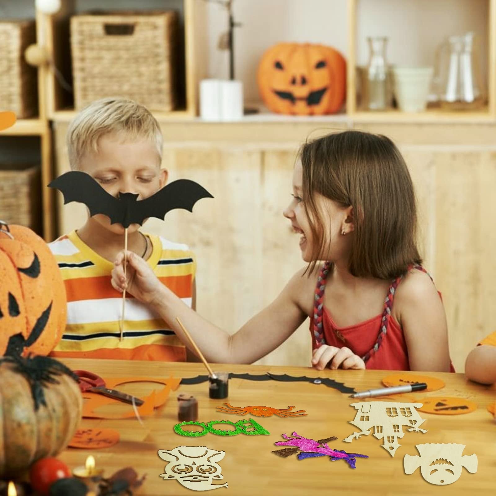 Children crafting Halloween wooden ornaments, one holding a bat cutout, others painting on a table with pumpkins and craft supplies.
