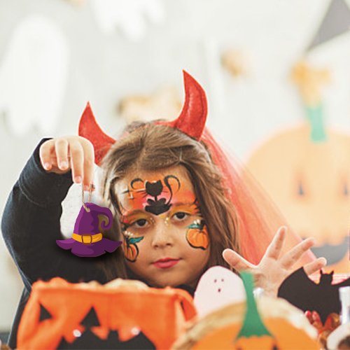 Child with Halloween face paint and devil horns holds up a purple witch hat ornament.