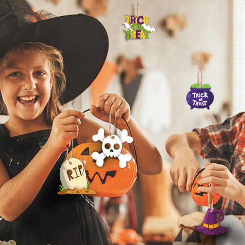 Children holding Halloween pumpkin buckets with assorted wooden ornaments like skulls, gravestones, and witch hats.