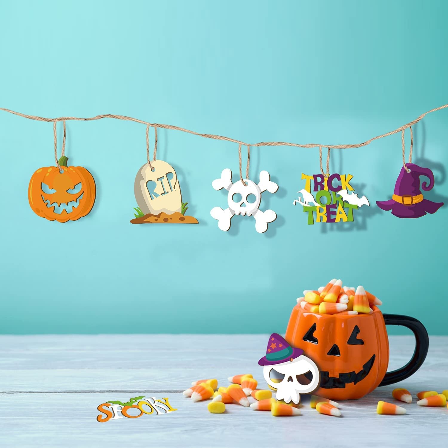 Halloween decorations including a pumpkin, tombstone, skull, witch hat, and 'Trick or Treat' sign hanging on a string, with a pumpkin mug filled with candy corn and scattered candy corn on a table.
