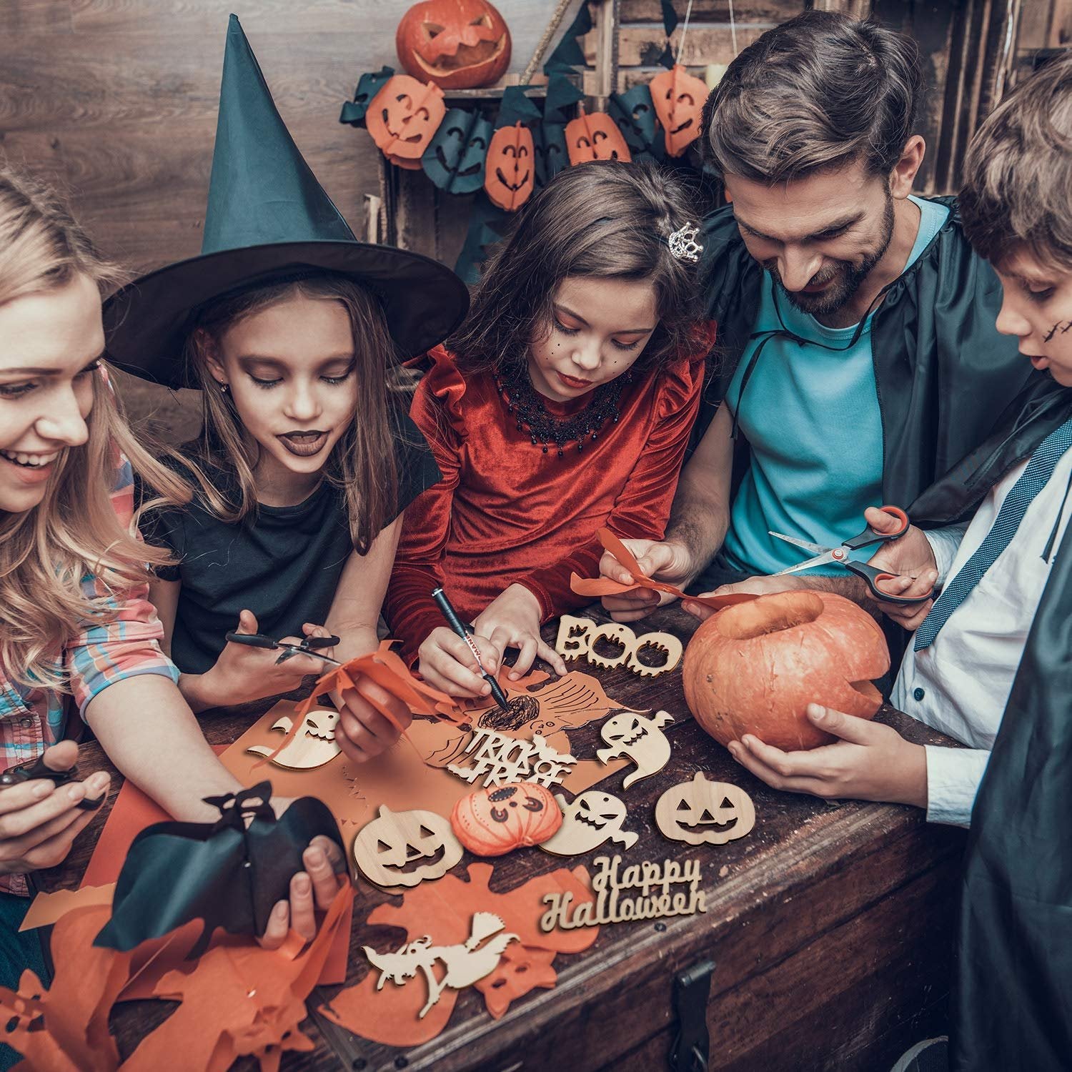 Family crafting Halloween decorations with wooden cutouts and pumpkins on a wooden table.