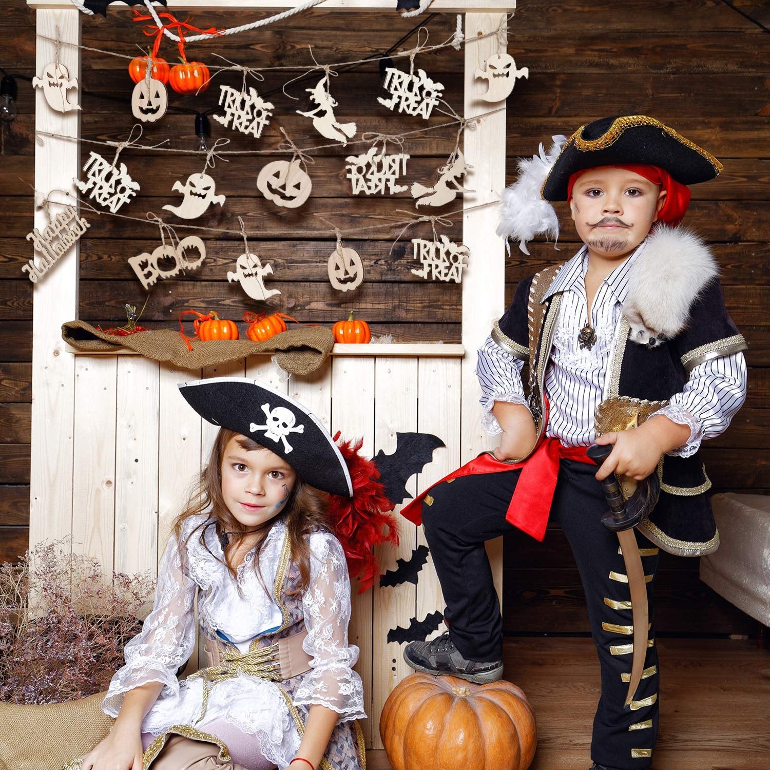Two children in pirate costumes posing in front of a wooden wall decorated with Halloween ornaments and pumpkins.