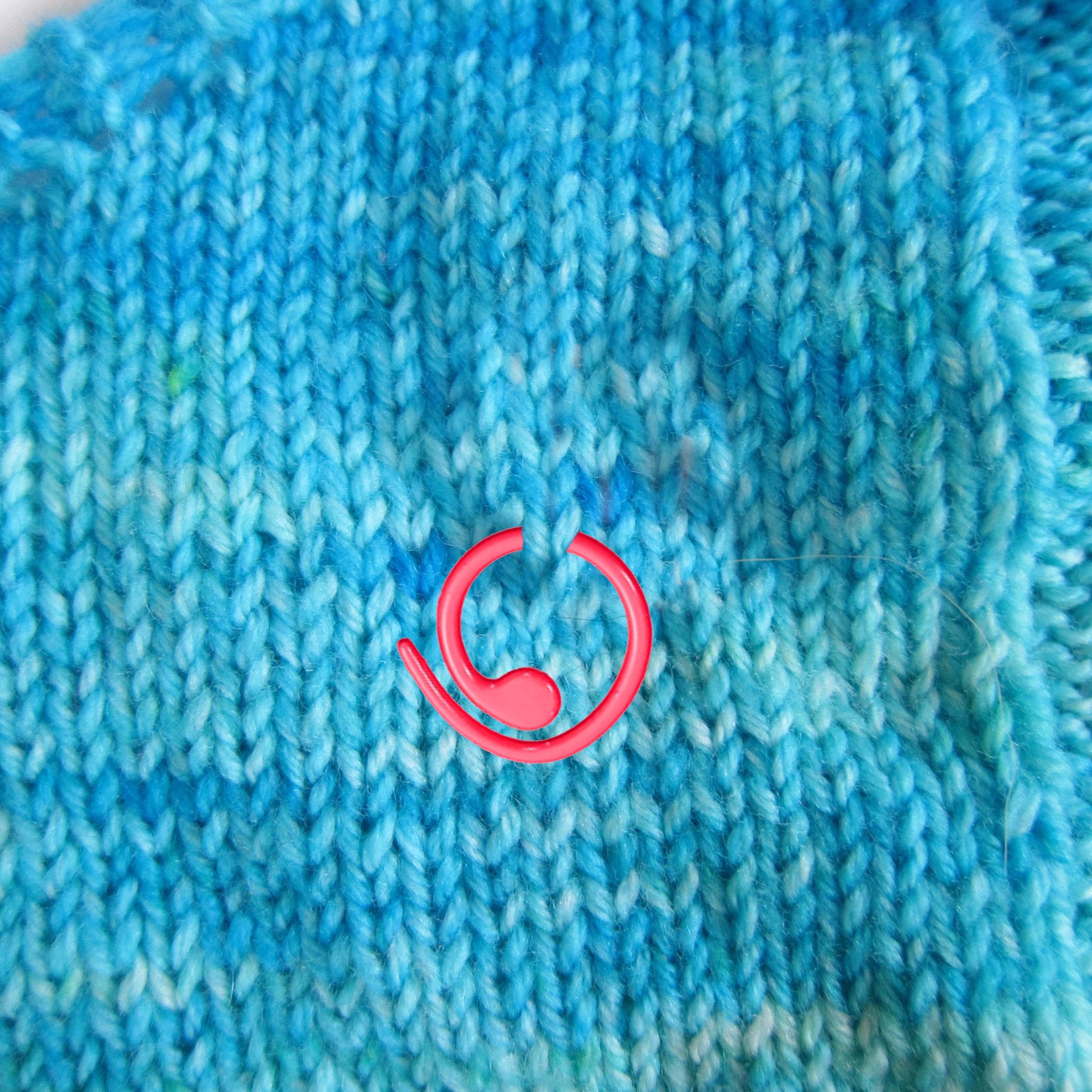 Close-up of a red stitch marker on blue knitted fabric