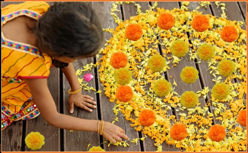 Child arranging orange and yellow artificial marigold flowers on a wooden deck, creating a decorative pattern.