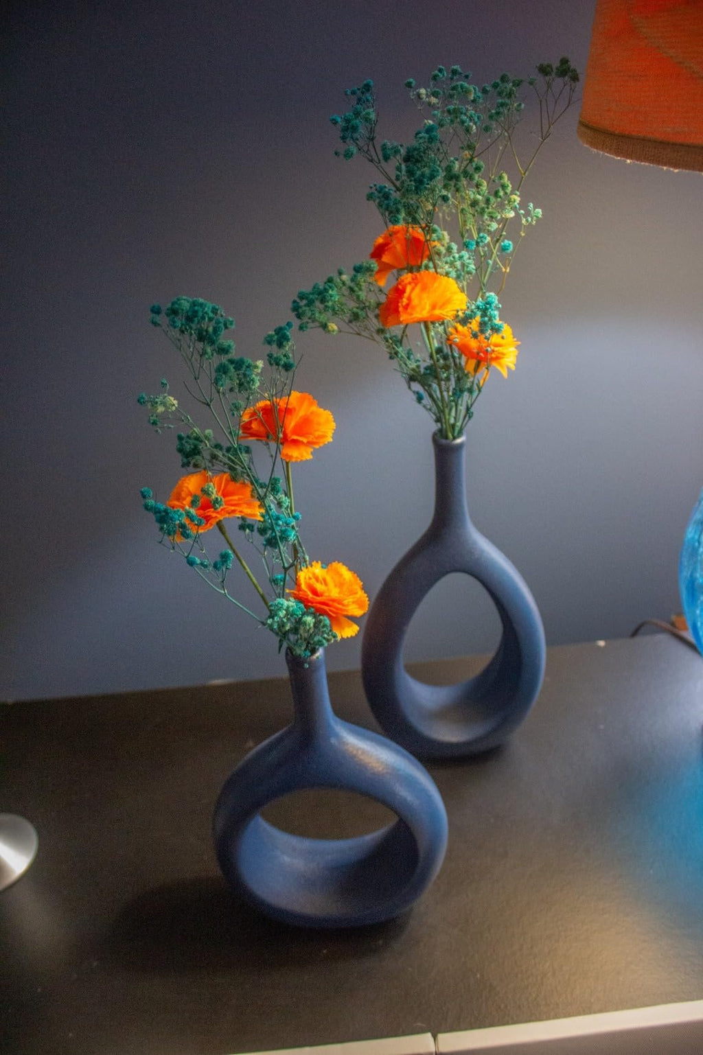 Two dark blue vases holding orange marigold flowers and green filler flowers on a dark surface.