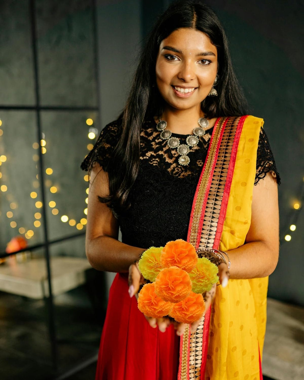 Woman in traditional Indian attire holding a small bunch of orange artificial marigold flowers