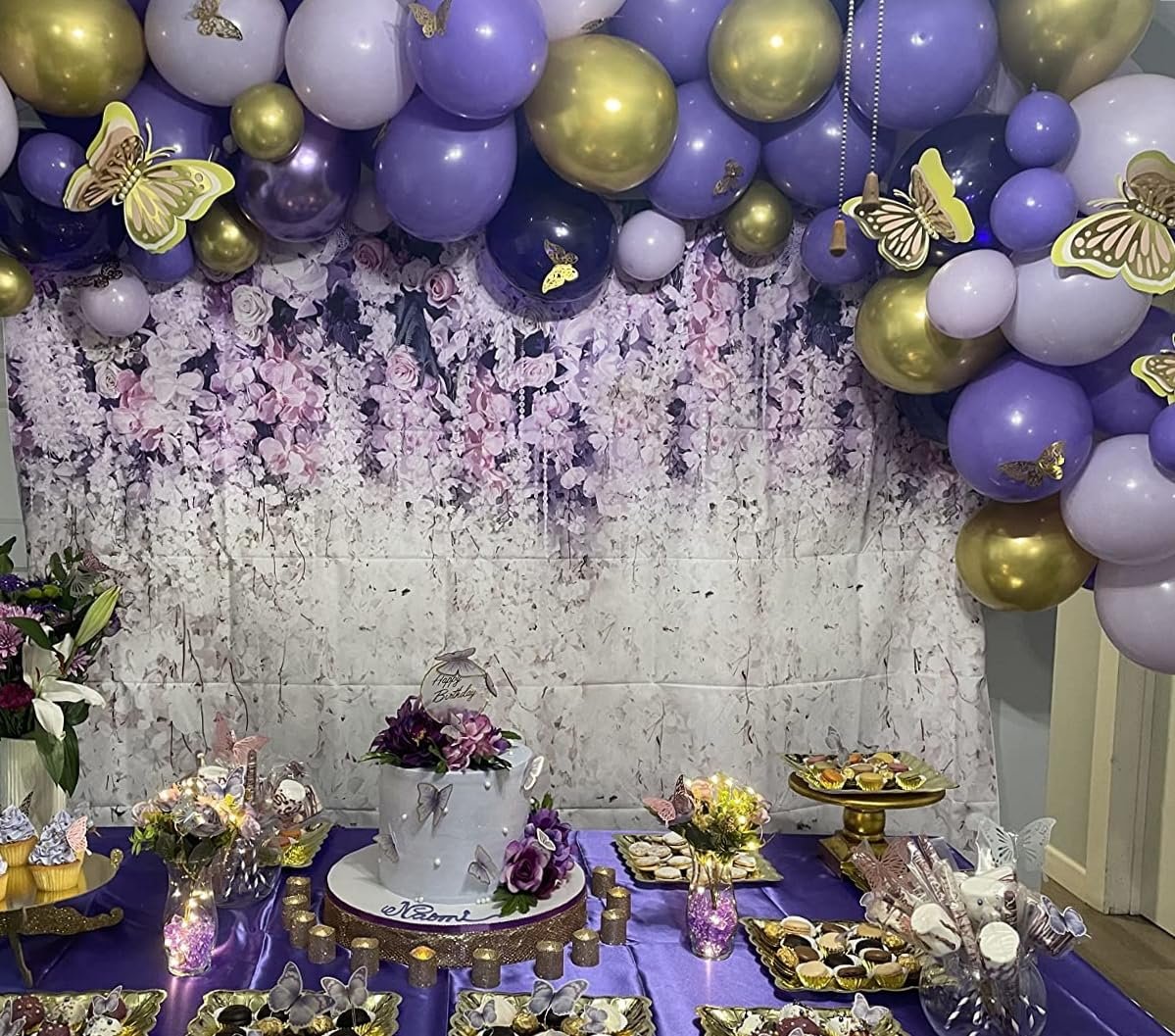 Purple and gold balloon arch over a dessert table with a cake, cupcakes, and cookies, decorated for a party.