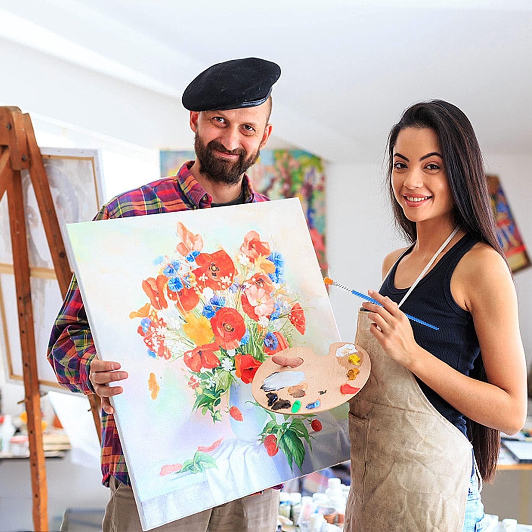 Man and woman in art studio holding a painting of flowers, woman holds paintbrush and palette
