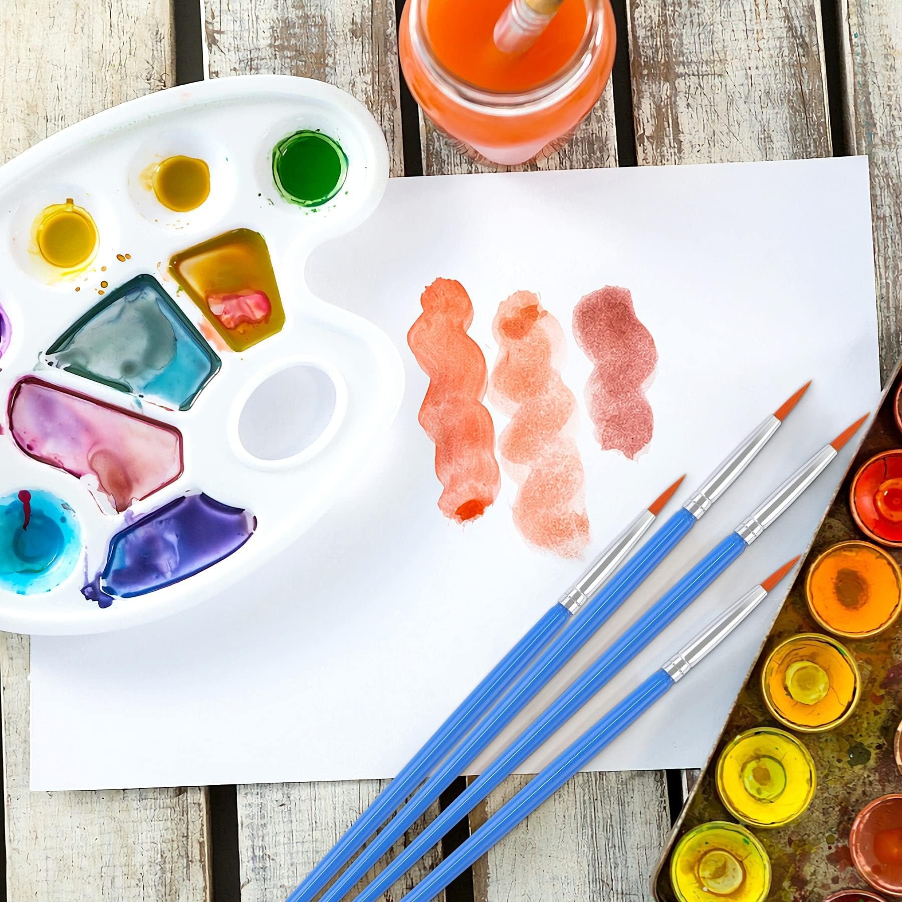 Watercolor painting setup with brushes, paint palettes, and paper with swatches