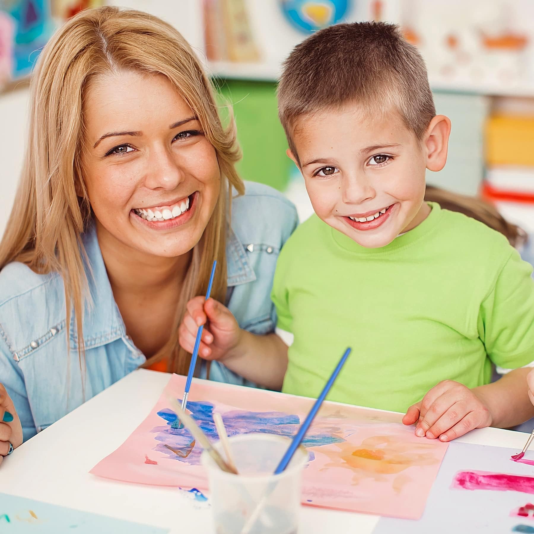 Woman and child smiling while painting with small brushes on paper