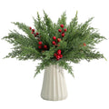 Artificial pine branches with red berries in a white vase, isolated on white background.