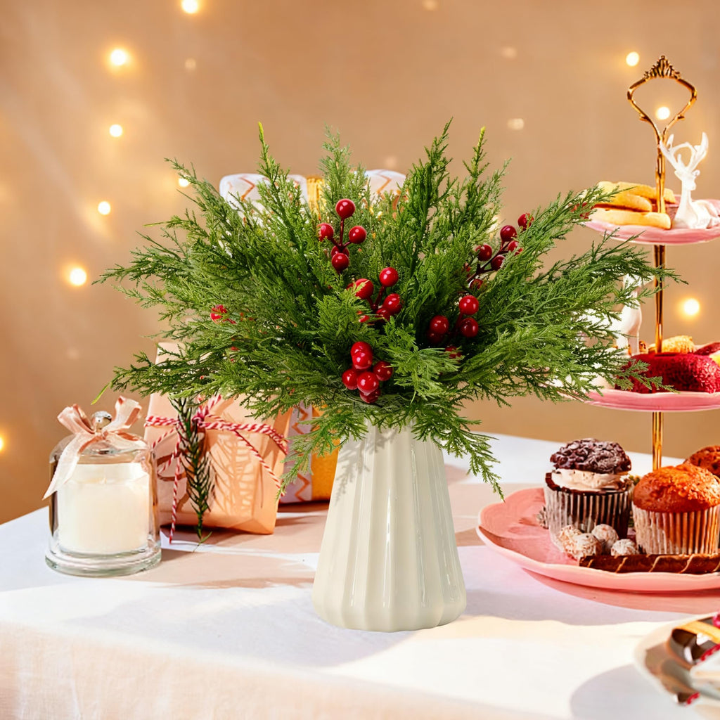 Artificial pine branches with red berries in a vase on a table with gifts and cupcakes