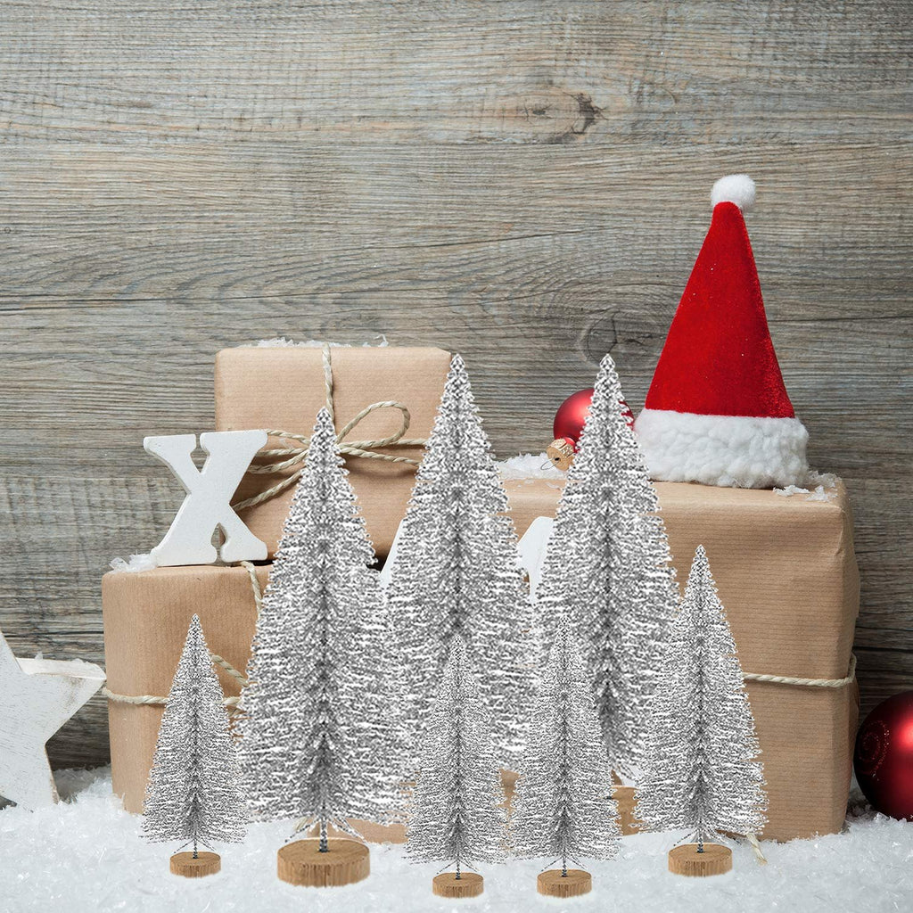 Silver glitter bottle brush Christmas trees arranged in front of wrapped gifts with a Santa hat and ornaments on a wooden background.