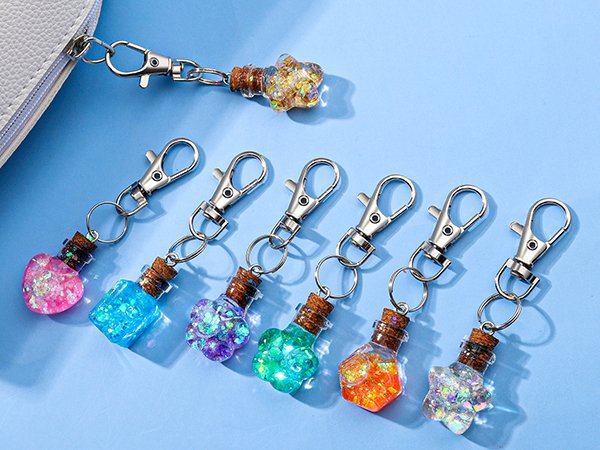 Assortment of colorful glitter-filled bottle-shaped charms with silver lobster clasps attached to a white zippered pouch.
