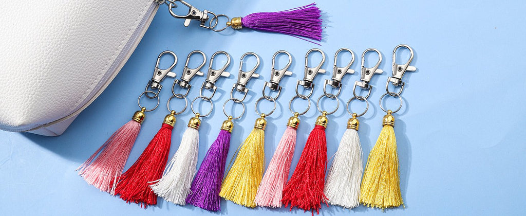 Assortment of colorful tassels with silver lobster claw clasps and key rings, next to a white pouch.
