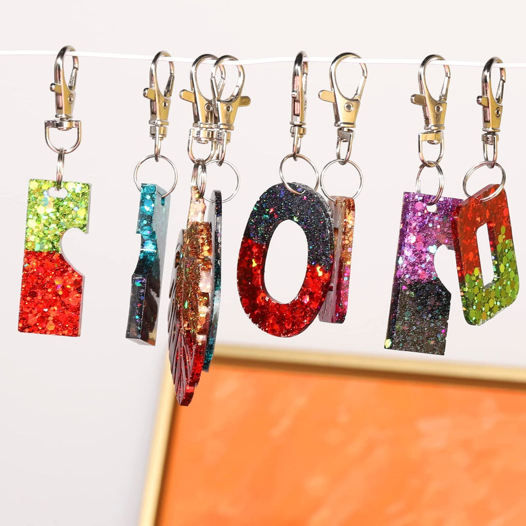 Assortment of glitter-filled resin keychains in various shapes and colors hanging on a wire