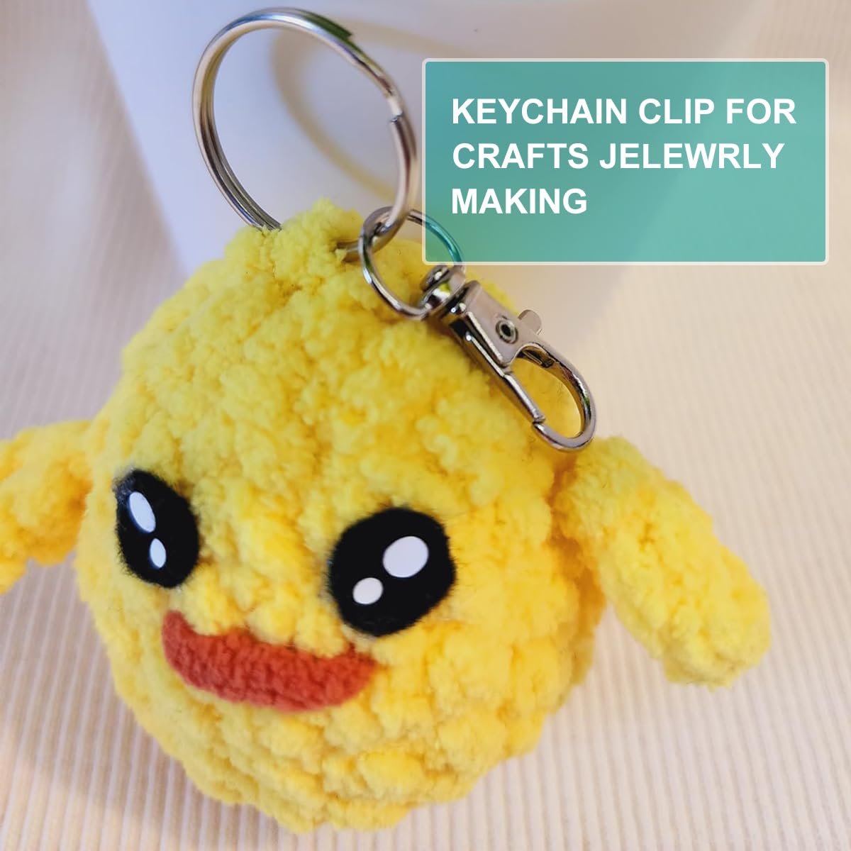 Yellow crocheted duck keychain with black eyes and orange mouth, attached to a silver clasp and ring.