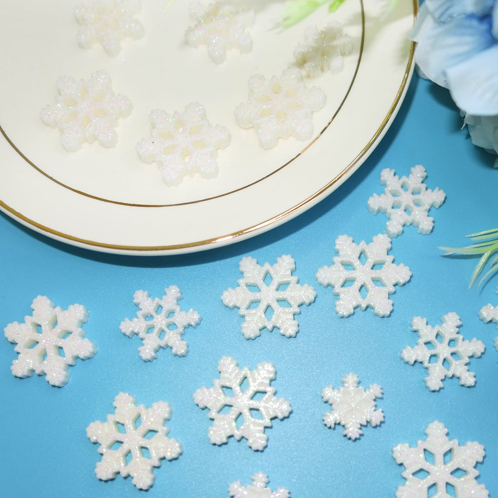 White glitter resin snowflakes in three sizes scattered on a blue surface and a plate.