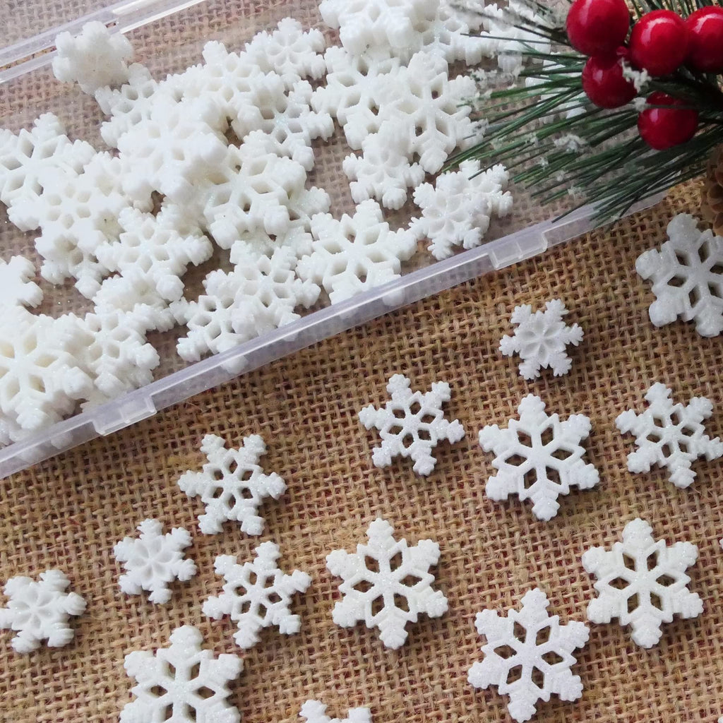 White glitter resin snowflakes in three sizes scattered on burlap with pine sprigs and red berries