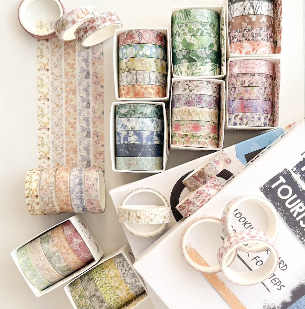 Collection of floral washi tape rolls in various patterns and colors, arranged in boxes and stacks.