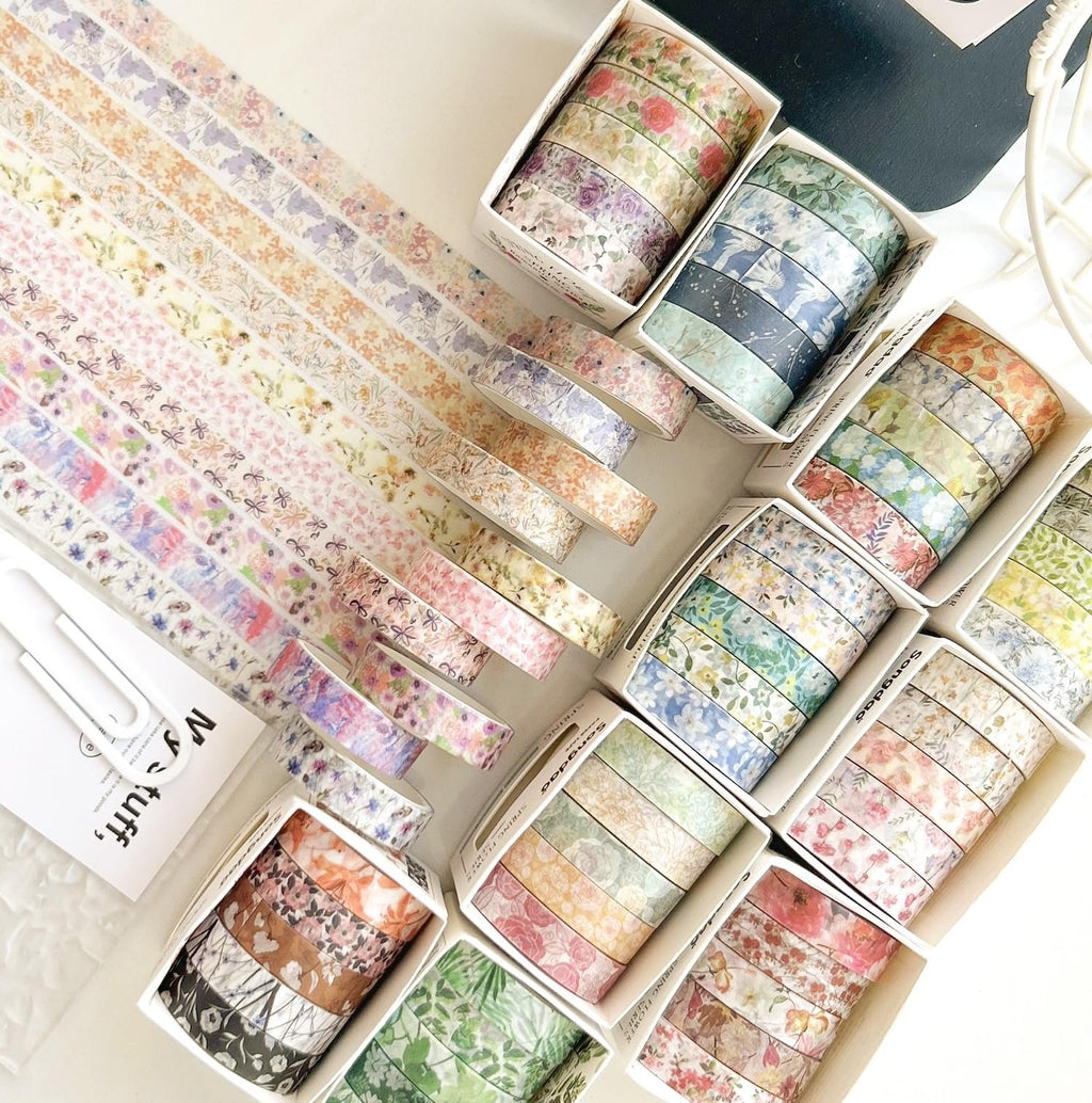 Collection of floral washi tape rolls in various pastel and muted colors, arranged in boxes and fanned out on a white surface.