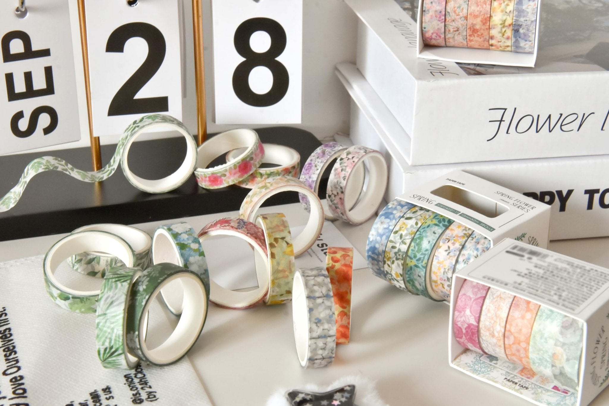 Assortment of floral patterned washi tape rolls scattered on a surface with a calendar and boxes.