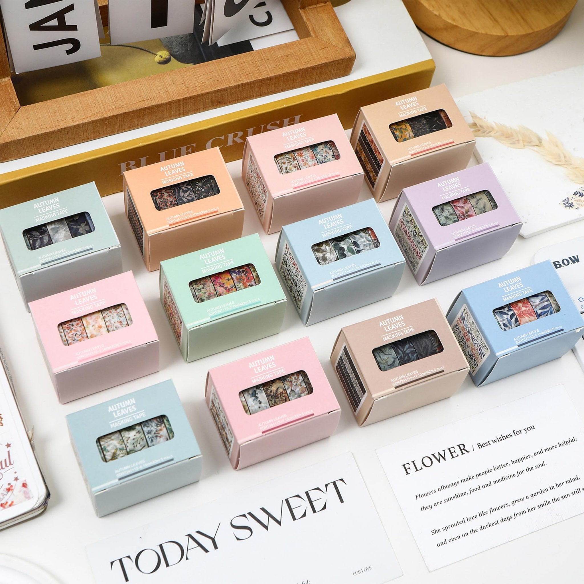 Collection of colorful masking tape boxes with floral and leaf patterns, arranged on a white surface with decorative cards.
