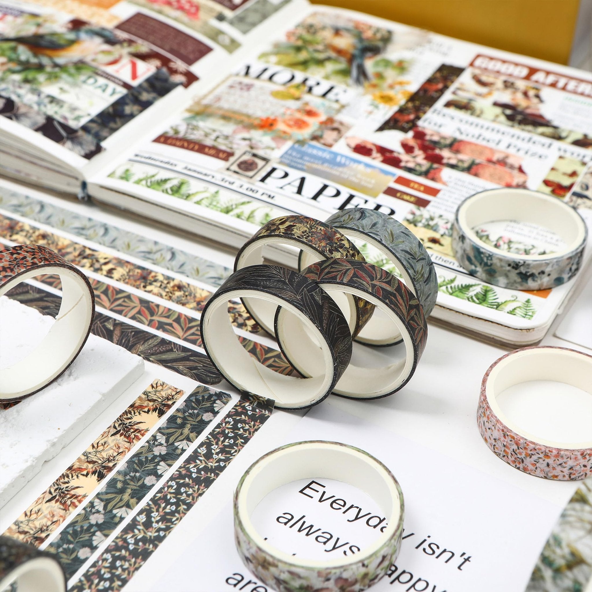 Assortment of floral and leaf patterned washi tape rolls arranged around an open journal with text and images.