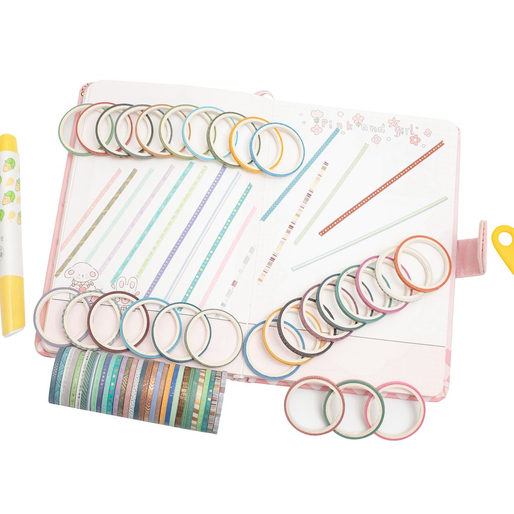 Assortment of skinny gold foil washi tape rolls arranged on an open journal with decorative lines and images.