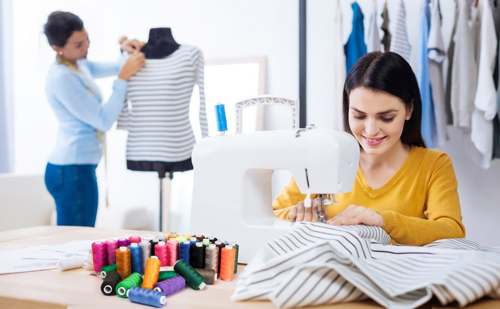 Woman sewing with a machine, surrounded by colorful spools of thread and a mannequin with a striped shirt.