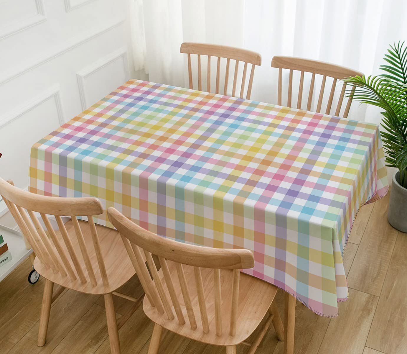 Pastel buffalo check plaid tablecloth draped over a dining table with chairs and a plant.