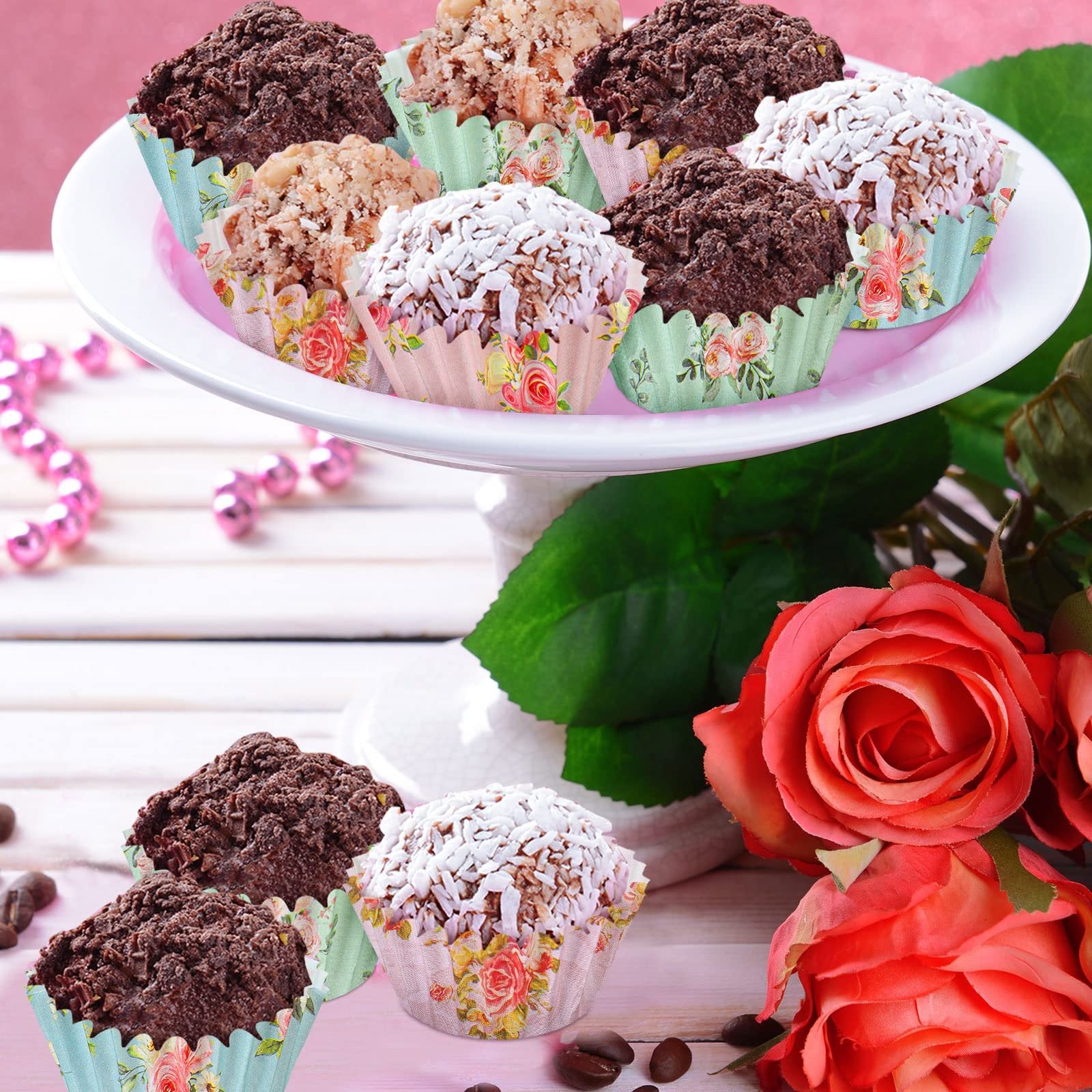 Mini cupcakes in floral patterned liners on a white cake stand with roses and coffee beans