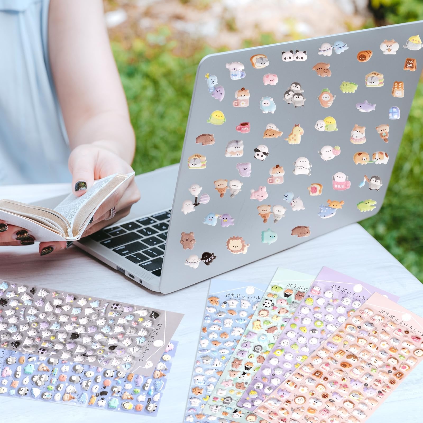 Person decorating a laptop with puffy 3D cartoon animal stickers, with sticker sheets fanned out on a table.