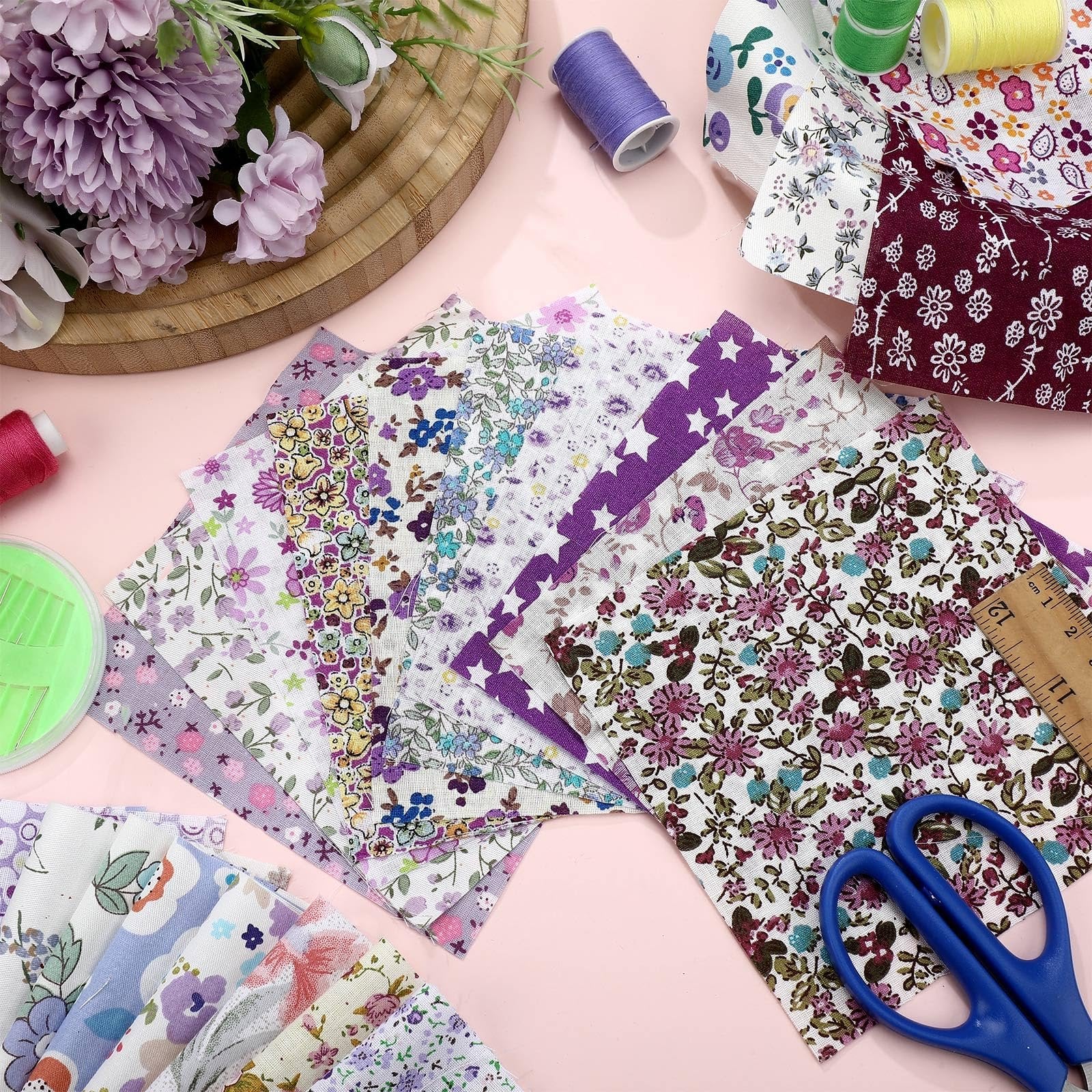 Assorted floral print fabric squares fanned out with sewing notions and scissors on a pink background
