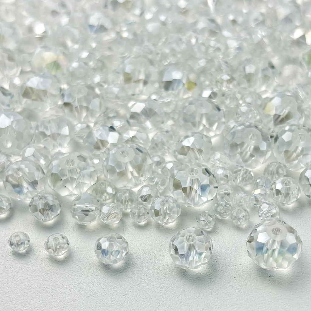 Pile of clear faceted rondelle glass beads in various sizes on a white surface