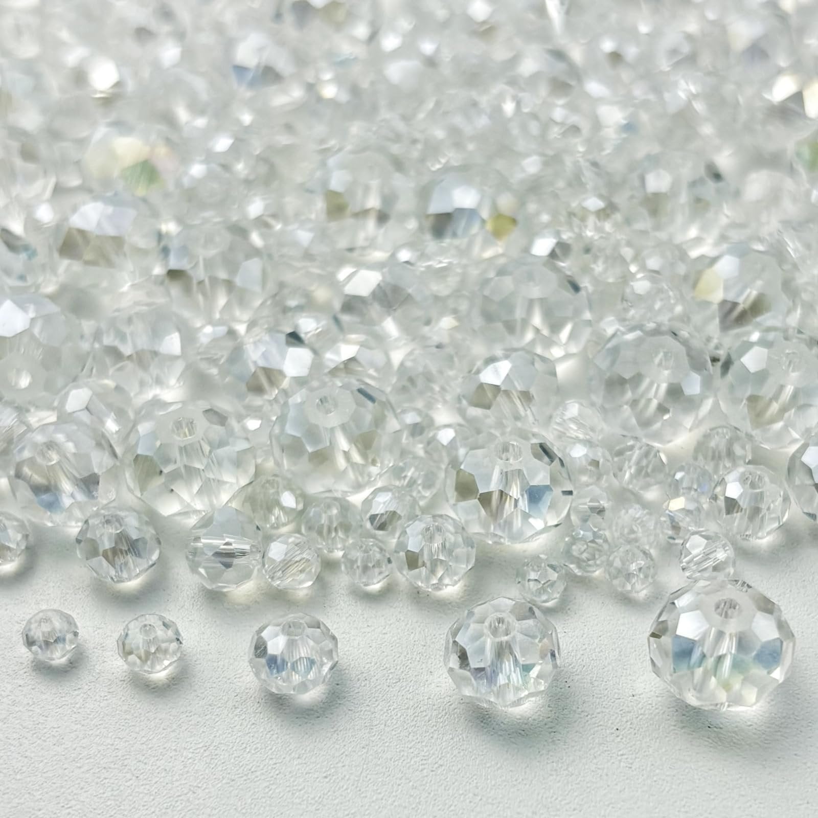 Pile of clear faceted rondelle glass beads in various sizes on a white surface