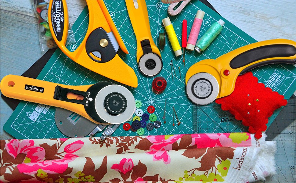 Sewing tools including rotary cutters, thread spools, buttons, pins, and fabric laid out on a cutting mat.