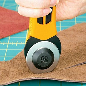 Hand holding a 60mm rotary cutter cutting brown fabric on a blue cutting mat