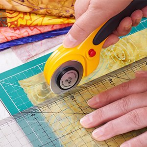 Person using a yellow rotary cutter with a 60mm blade to cut fabric along a ruler on a green cutting mat.