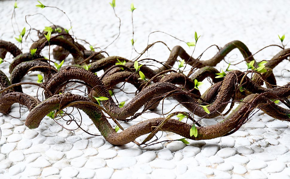 Bendable artificial tree vine garland with green shoots laid on a white pebble surface, close-up view.