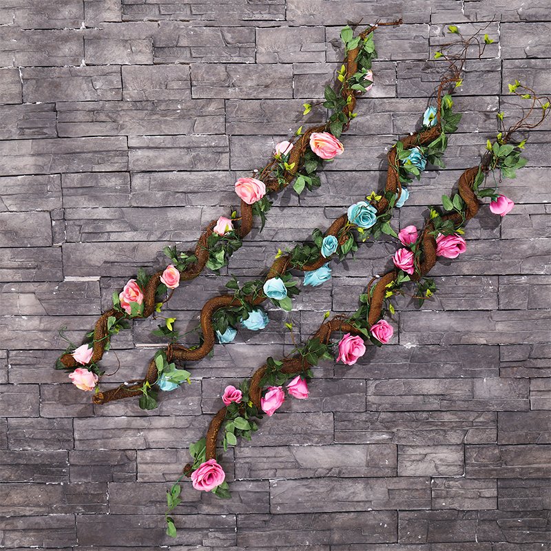 Three bendable artificial tree vine garlands with pink and blue roses against a gray stone wall.