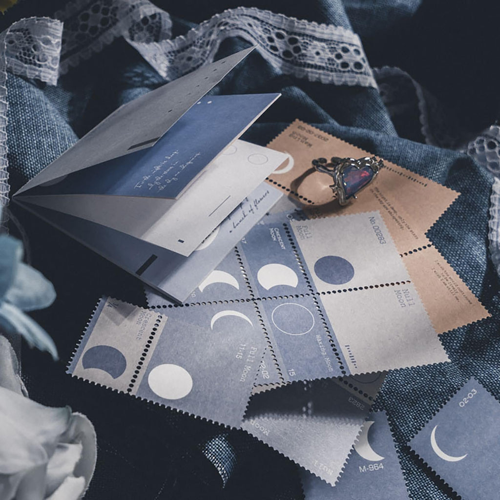 Scrapbook embellishment papers with moon phase designs and vintage text, arranged with a ring and lace.