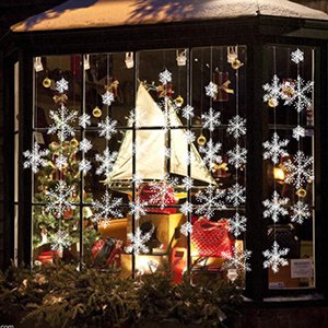 White Christmas snowflake ornaments and gold baubles decorating a window display with a sailboat model and gifts inside.