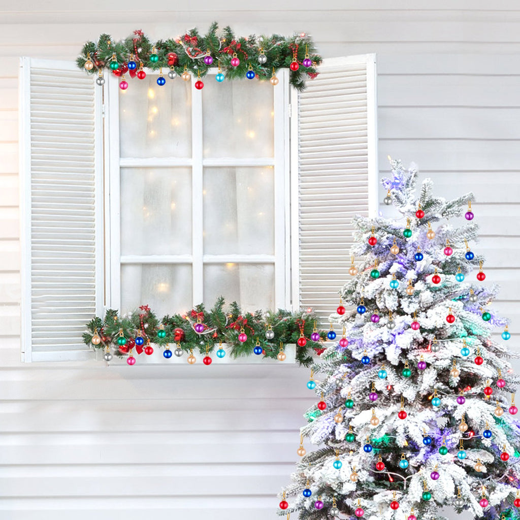 Mini Christmas balls ornaments in various colors decorating a flocked Christmas tree and a window garland