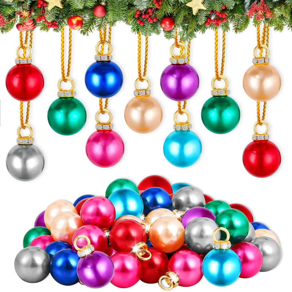 Assortment of colorful mini Christmas ball ornaments with gold hanging loops and rhinestone accents, displayed on a white background with a festive green garland above.