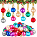 Assortment of colorful mini Christmas ball ornaments with gold hanging loops and rhinestone accents, displayed on a white background with a festive green garland above.