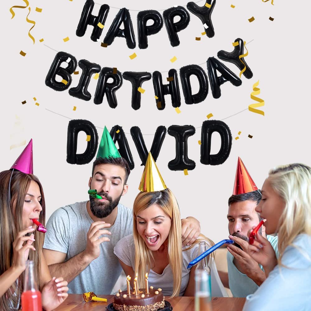 Group of friends celebrating a birthday with black foil balloons spelling 'Happy Birthday David' and confetti.