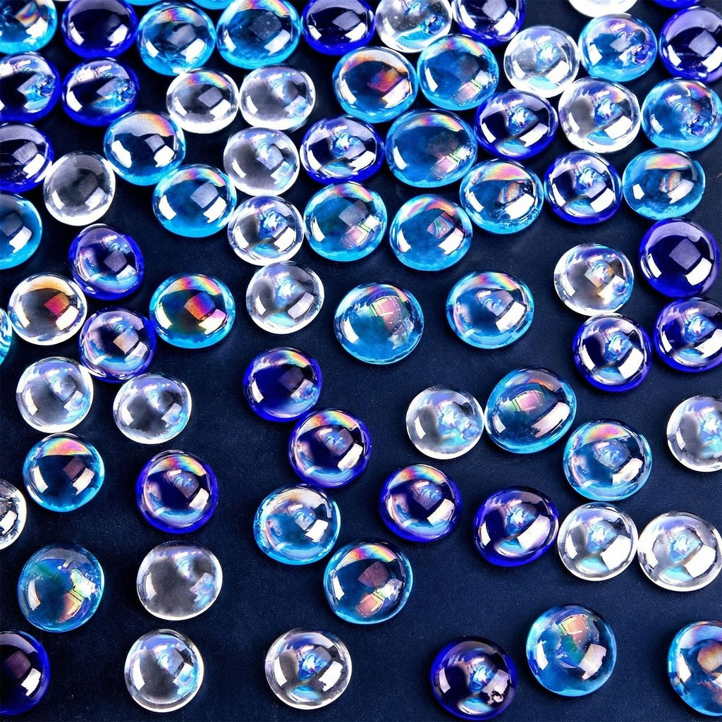 Flat iridescent blue glass marbles scattered on a dark blue surface, showing clear and deep blue colors with rainbow reflections.